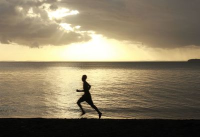 Silhouette man on beach against sky during sunset