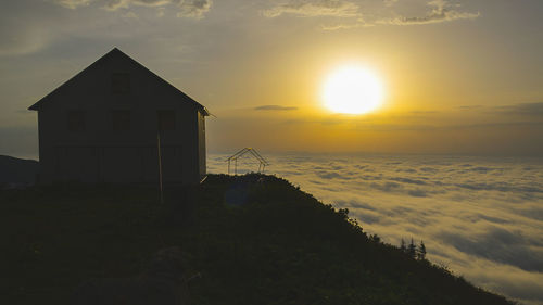 Silhouette house on building against sky during sunset