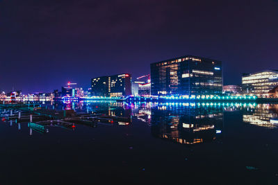 Illuminated buildings by river against sky at night