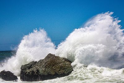 Waves splashing on rocks against blue sky