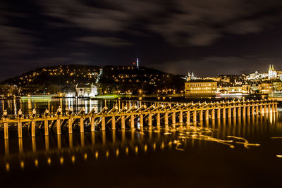 Illuminated buildings by river against sky at night