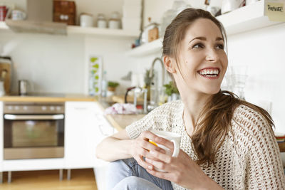 Happy young woman with cup of coffee in kitchen