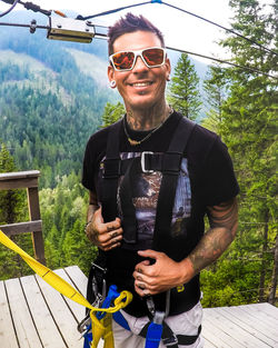 Portrait of young man wearing sunglasses standing against trees