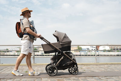 Caucasian man, father carrying little newborn baby in carrier with stroller,family traveling 