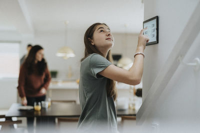 Girl adjusting room temperature through digital tablet mounted on wall at home