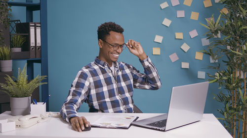 Smiling businessman using laptop against wall