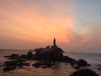 Statue on beach against sky during sunset