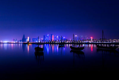 Illuminated city by river against sky at dusk