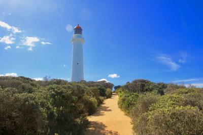 Lighthouse amidst trees and buildings against sky