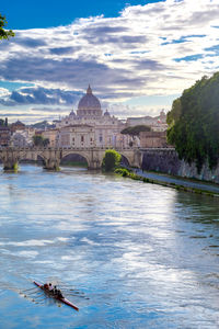 Arch bridge over river by buildings against cloudy sky