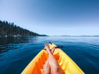 Low section of woman sitting in boat on lake against clear blue sky