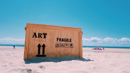 Wooden box with text at sandy beach on sunny day