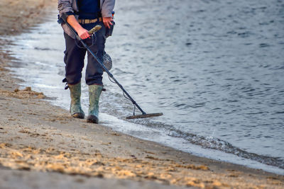 Low section of man with metal detector walking on beach