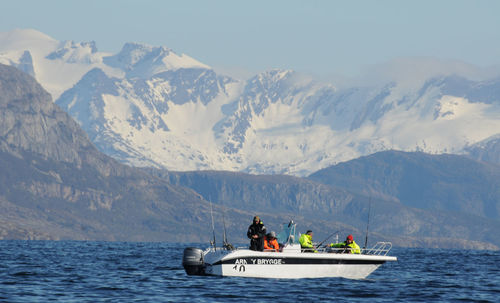 People on boat in sea by mountains against sky