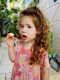 Portrait of cute girl standing against wall eating apple