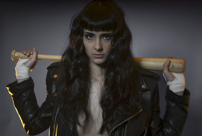 Portrait of young female model holding baseball bat against gray background