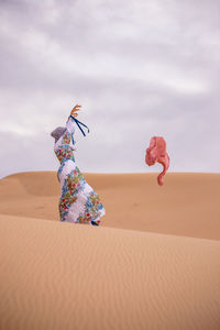 Lady in colorful dress releasing pink scarf in to the air the middle of sand dune in desert.