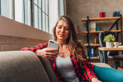 Young woman using mobile phone while sitting on sofa at home