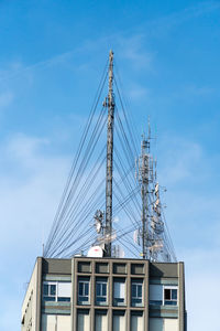 Low angle view of crane by building against sky