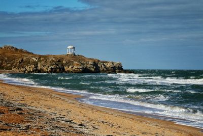 Lighthouse on beach by sea against sky