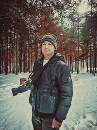 Portrait of man with camera standing in snow covered forest