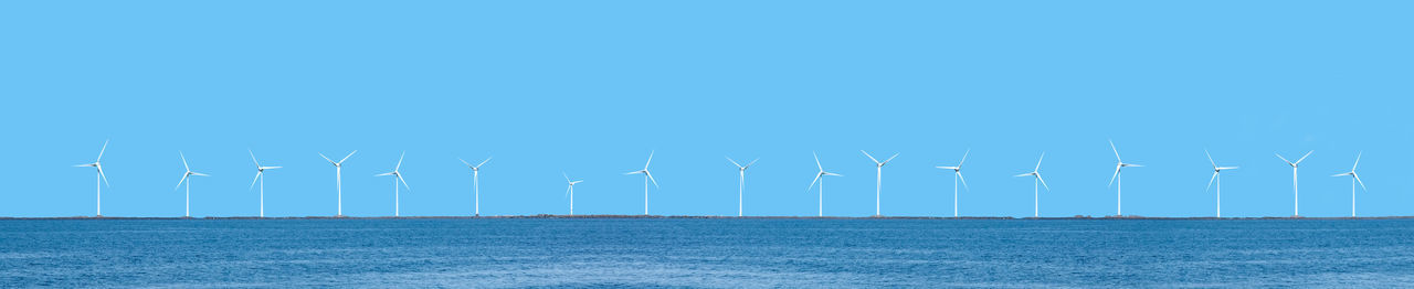 Wind turbines in sea against blue sky