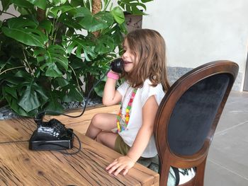 Smiling girl talking on rotary phone while sitting on chair at home