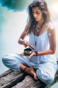 Woman holding singing bowl while doing yoga at lake