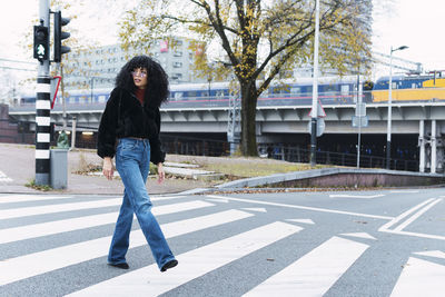 Fashionable woman crossing street on road marking in city