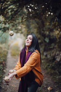 Young woman throwing fruits in air while standing in forest