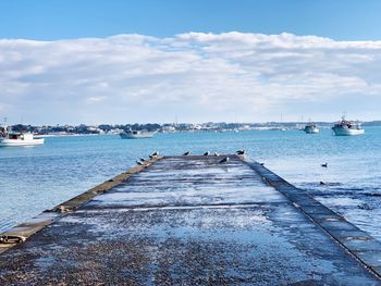 Sailboats moored on pier by sea against sky