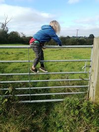 Rear view of boy on field by fence against sky