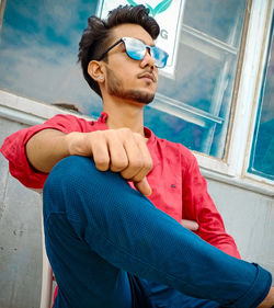 Young man looking away while sitting against wall