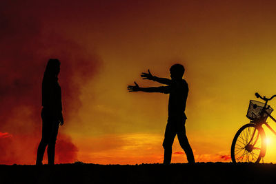 Silhouette people with bicycle standing on field against sky during sunset