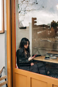 Long-haired brunette asian woman having a coffee oh a coffee shop while is looking a cellphone