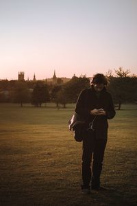 Young man looking at mobile phone on grassy field against clear sky