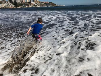 Rear view of boy playing at beach against sky