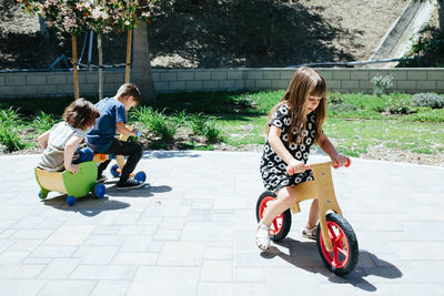 Three kids outside ride around on wooden bicycles