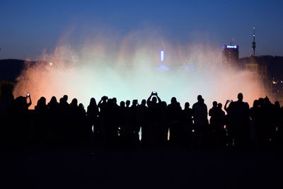 Silhouette people standing by fountain against sky at night