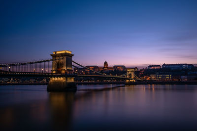 Illuminated bridge over river against sky during dusk