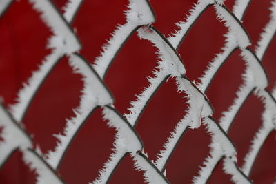 Full frame shot of frost on chainlink fence against red wall