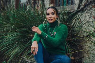 Portrait of young woman sitting on plants against trees