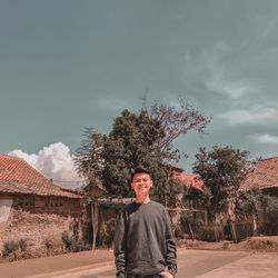 Portrait of man standing by tree against sky