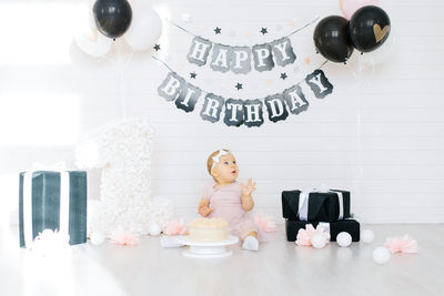 A one-year-old girl sits near a cake, celebrates her first birthday in a photo zone 