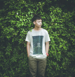 Young man looking away while standing against plants