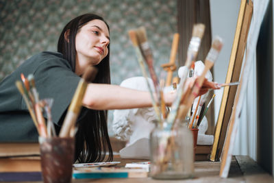 Young woman artist teenager girl student with dark long hair in casual draws picture at art studio