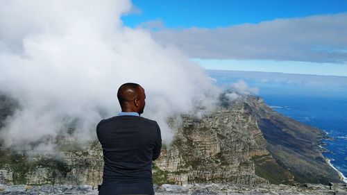 Rear view of man standing on mountain against sky