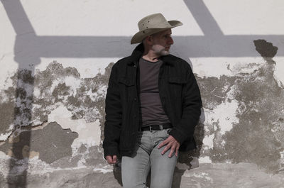 Portrait of adult man in cowboy hat and jeans against wall with sunlight and shadow. almeria, spain