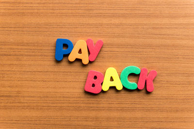 High angle view of colorful pay back text on wooden table