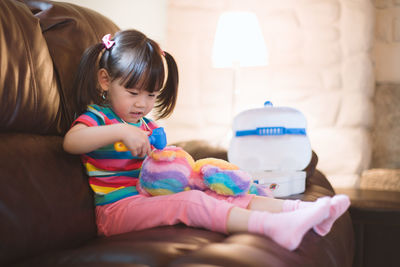 Young girl pretend play as doctor looking after her bear paient in the living room